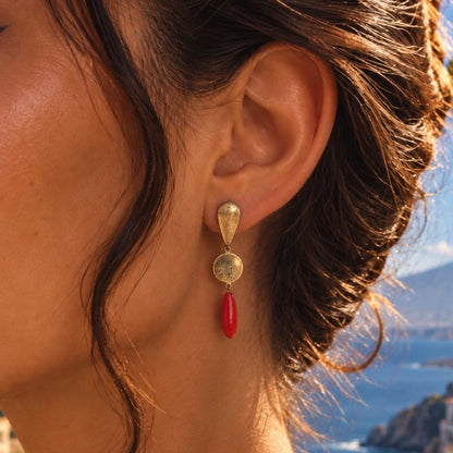 Woman wearing a Sardinian red coral and 925 silver drop earring with gold-tone geometric details against a coastal backdrop.
