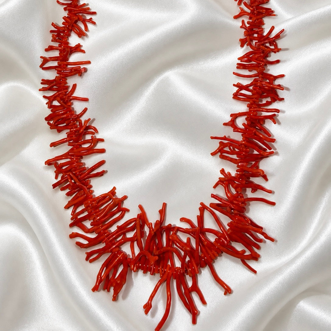 Red necklace with coral-shaped branches arranged on white satin, featuring longer branches at the center.