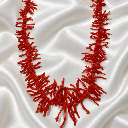 Red necklace with coral-shaped branches arranged on white satin, featuring longer branches at the center.