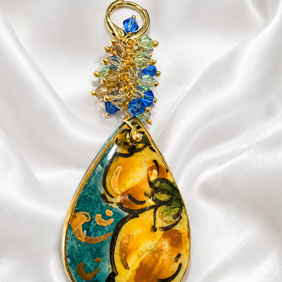 Macro close-up of handmade Sicilian ceramic drop earring with hand-painted lemon motif, gold lustre and Swarovski crystals