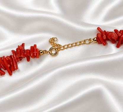 Close-up of the gold-tone spring ring clasp and extension chain on a red branch-style necklace, resting on white satin.