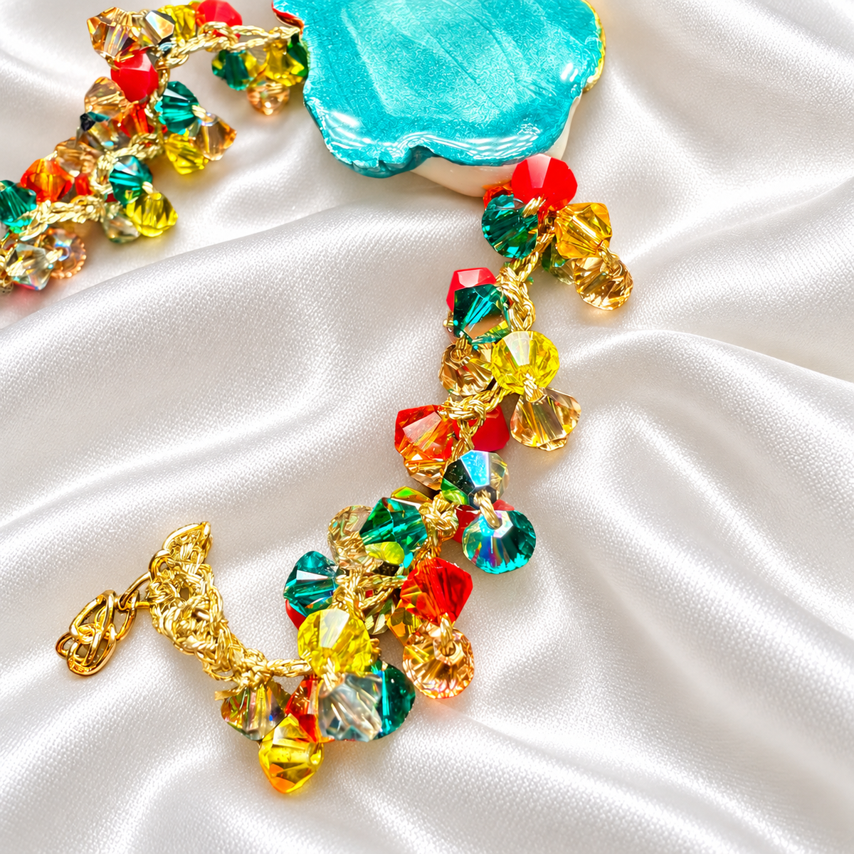 Close-up of handmade Sicilian bracelet featuring multicolored Swarovski crystals, a gold-plated brass chain and hand-painted ceramic Moor’s Head on white satin.
