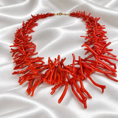 Angled view of a red necklace with coral-shaped branches and a gold-tone clasp, displayed on white satin.