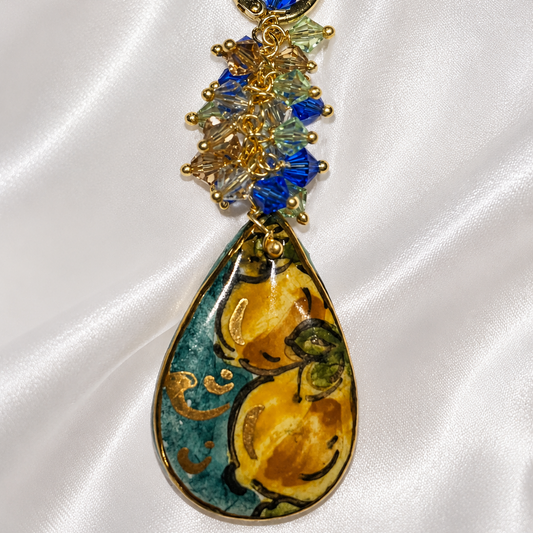 Close-up of handmade Sicilian drop earring with hand-painted Caltagirone ceramic lemon motif, gold lustre and blue Swarovski crystals