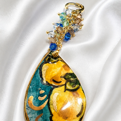 Macro close-up of handmade Sicilian ceramic drop earring with hand-painted lemon motif, gold lustre and Swarovski crystals