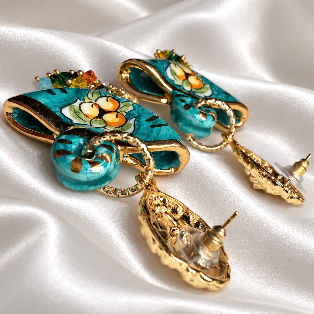 Side close-up of turquoise Caltagirone ceramic coffa earrings, showing hollow interiors, gold rims, and stud posts with clear disc backs.