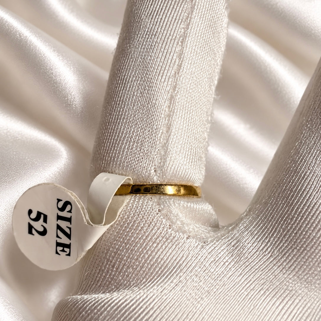 Rear view of a polished gold-tone ring band on a white satin glove, with a size 52 tag attached.