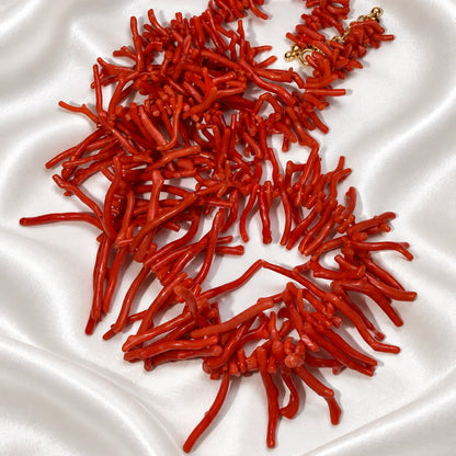 Red necklace loosely arranged on white satin, showing glossy coral-shaped branches in varying lengths and a gold-tone clasp.