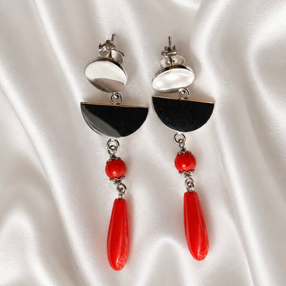 Sardinian red coral and rhodium-plated silver earrings with oval studs, semicircle links, and red bead drops on white satin.