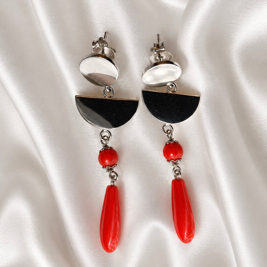 Sardinian red coral and rhodium-plated silver earrings with oval studs, semicircle links, and red bead drops on white satin.