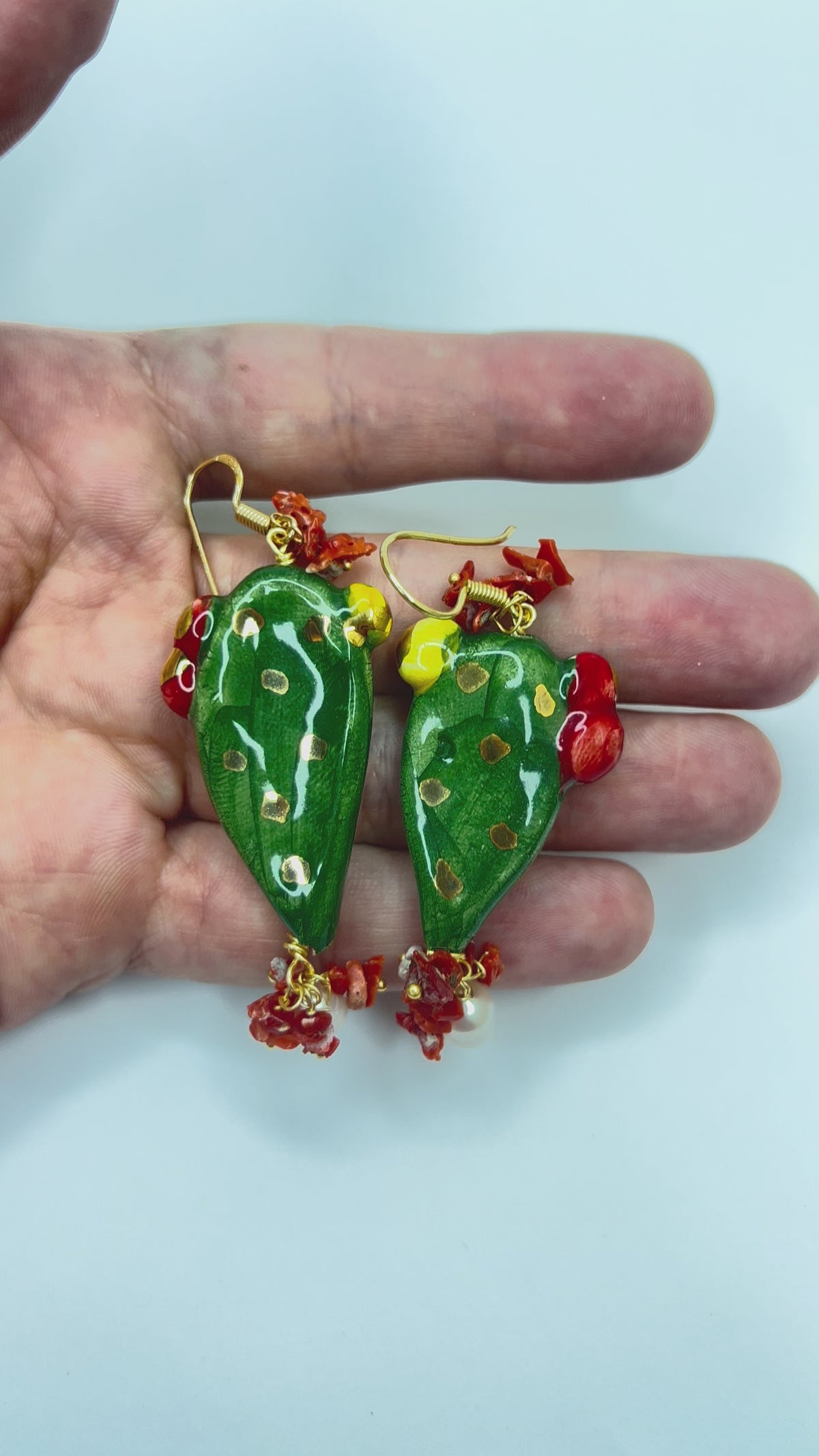 Video showing handmade Sicilian prickly pear earrings in hand-painted Caltagirone ceramic with red coral and freshwater pearls held in hand