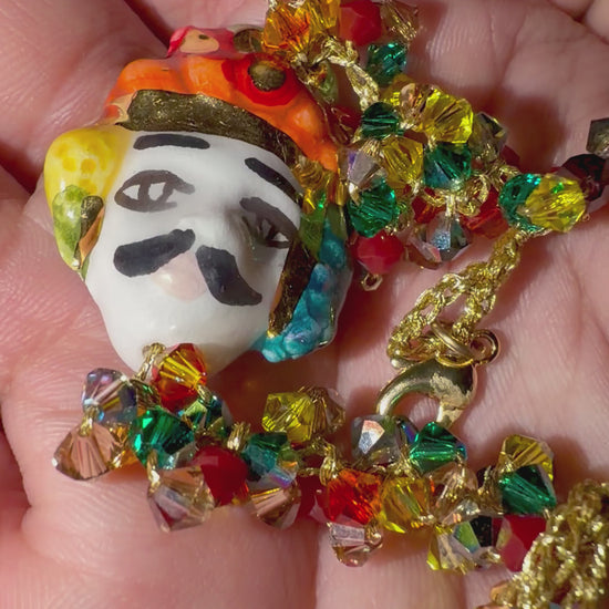 Close-up video of a handmade Sicilian bracelet featuring a hand-painted ceramic Moor’s Head with 15% gold lustre, multicolored Swarovski crystals and a gold-plated brass chain.
