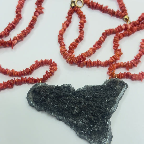 Video close-up of Sicily-shaped Mount Etna lava stone pendant held in hand with Mediterranean red coral necklace
