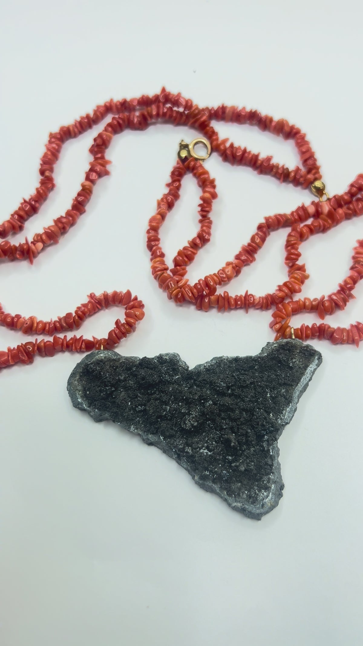 Video close-up of Sicily-shaped Mount Etna lava stone pendant held in hand with Mediterranean red coral necklace
